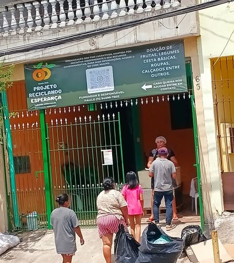 Fachada da sede do Projeto Reciclando Esperança, com a placa do projeto sobre o portão verde e pessoas chegando com sacolas de doação.
